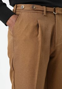Bruine op maat gemaakte broek met een gestructureerde finish, voorzien van twee plooien aan de voorkant, twee knopen aan de tailleband en zijzakken.