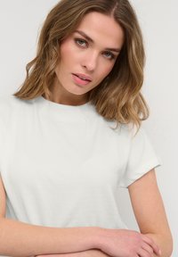T-shirt bianco a maniche corte, collo tondo, texture liscia, design aderente, con lievi variazioni nello spessore del tessuto. Nessuni motivi o accenti visibili.