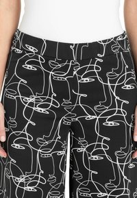 Pantaloni neri con un disegno continuo di volti astratti in linea bianca. Il design ha una texture liscia e una vita elastica.