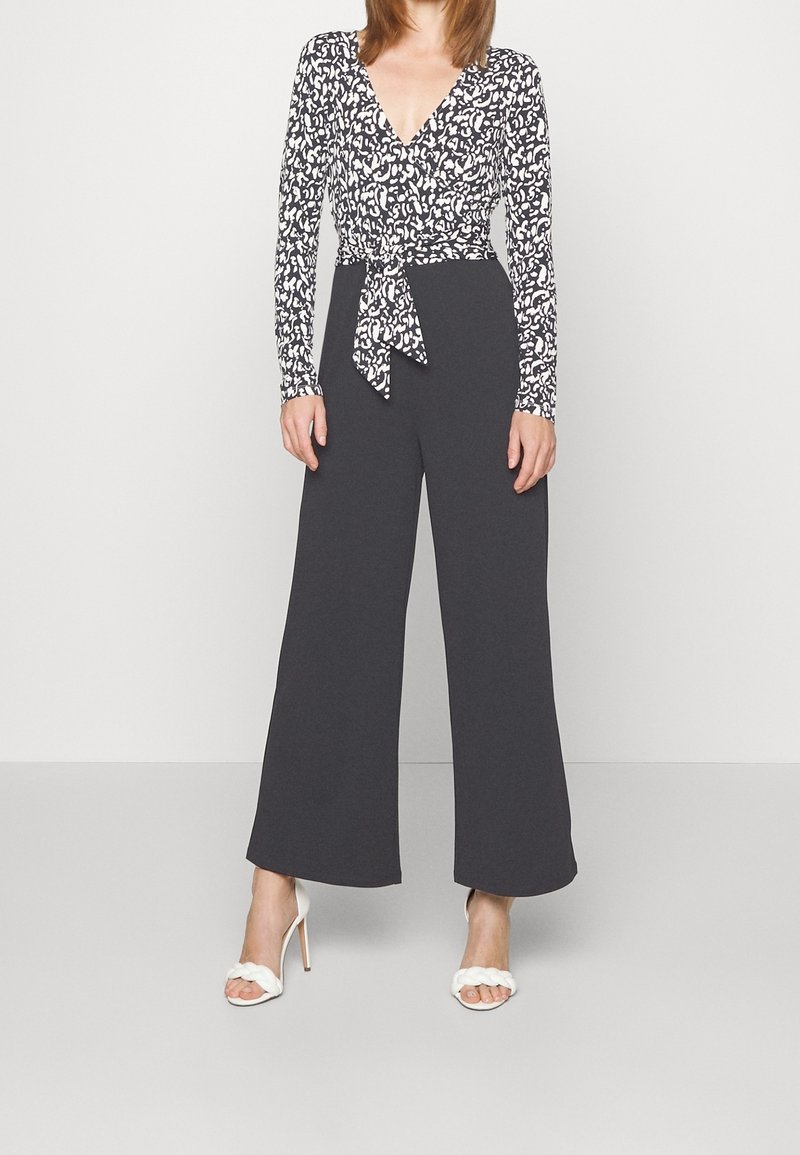 Top de manga larga con estampado en blanco y negro, combinado con pantalones anchos de color gris oscuro. Presenta un lazo en la cintura y una tela texturizada.