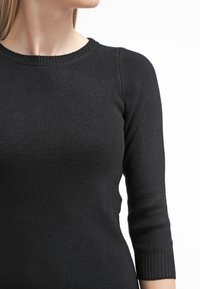 Svart ribbad stickad tröja med rund halsringning och trekvartsärmar, som visar en slät textur och en figurnära silhuett.