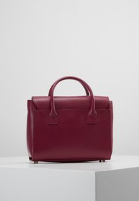 Burgundy läderhandväska med strukturerad design, dubbla handtag ovanpå, texturerad yta och lockstängning. Kompakt med en minimalistisk look.