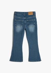 Jeans med utställd nederkant i medelblått, med en läderpatch i tan, fem fickor och lätt blekning på baken och låren.