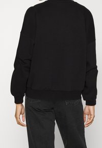 Sudadera de algodón negra con ajuste relajado, cuello redondo y puños acanalados. Tejido texturizado con acabado liso, diseño minimalista.