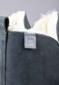 Dark green suede boot with a soft, white fur lining and a gray label that reads "LAKE LAND." Features stitched seams and a short height.