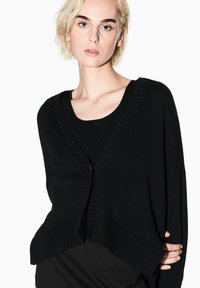 Cardigan nero lavorato a maglia con scollo a V profondo, bordi a coste e vestibilità morbida. Presenta una chiusura con un solo bottone e spacchi laterali.