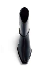 Bota de cuero negro con punta afilada y altura hasta la mitad de la pantorrilla, con una correa lateral y una hebilla de latón, mostrada desde una vista superior.