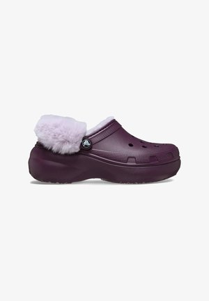 Zueco morado con un suave collar de pelaje sintético lavanda, que cuenta con orificios de ventilación y un acento de logo circular cerca del lado. Suela de goma texturizada.