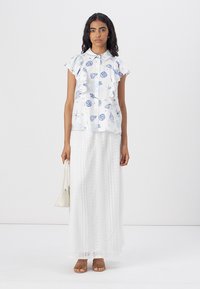 Hvit bluse med blå skjelltrykk, volanger på ermene og knapper foran. Kombinert med en hvit blonde maxi skjørt og brune sandaler.