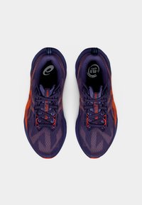 Zapatos deportivos morados con acentos naranjas, parte superior de malla, diseño texturizado y plantillas negras con logotipo, con cordones tradicionales.