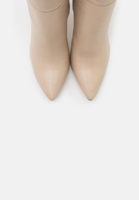 Beige skinnstövlar med ankelfot, spetsig tå, slät yta och minimal sömnad. Snygg, tight design med avsmalnande silhuett.