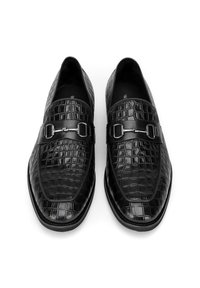 Zwarte leren loafers met een krokodillenpatroon, ovale neus en een band met zilverkleurige hardware over de wreef. Plat voetbed.