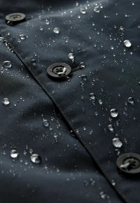 Material negru impermeabil cu picături pe suprafață, având butoane negre și un finisaj neted, texturat.