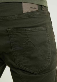 Olijfgroene broek met een gestructureerde afwerking, met een kenmerkend ontwerp van de achterzak en een leren merklabel met de tekst "CHASIN'."