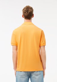 Oranssi polo paita, jossa on tekstuuri, lyhyet hihat ja klassinen kaulus, yhdistettynä vaaleansinisiin farkkuihin.