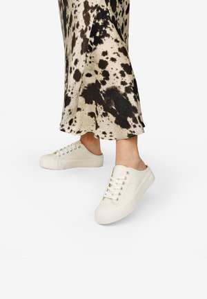 Zapatillas de lona en color crema con punta redondeada, diseño de cordones y suelas de goma, combinadas con una falda de lunares a la altura de la rodilla.