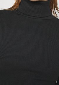 Schwarzer, gerippter Rollkragenpullover aus elastischem Stoff, der eine figurbetonte Passform und einen hohen Kragen aufweist und eine strukturierte Oberfläche zeigt.