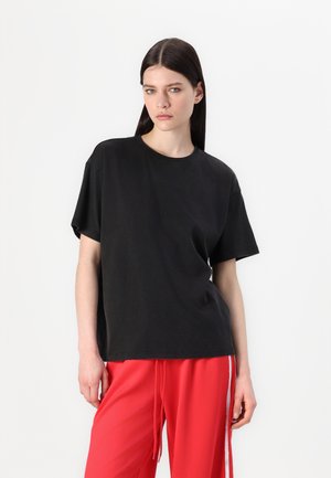 Zwart oversized katoenen t-shirt met korte mouwen en een ronde hals, gecombineerd met helderrode broek met trekkoord. Eenvoudig en casual ontwerp.