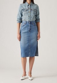 Denim jacket with button closure, four front pockets, paired with a high-waisted denim pencil skirt. Both in light blue. White slip-on shoes.