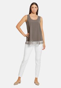 Ärmelloses, olivgrünes Top mit quadratischem Ausschnitt und filigranem Spitzenbesatz am Saum. Kombiniert mit weißen Skinny-Jeans und nudefarbenen Ballerinas.