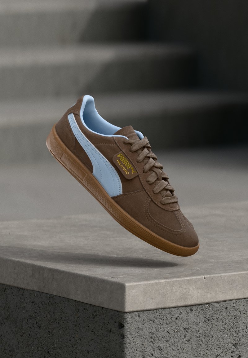 Pruunist sametist teki, millel on heledatest sinisest nahast detailid, kummist põhi ja beežid kengid. Küljel on bränditud silt.