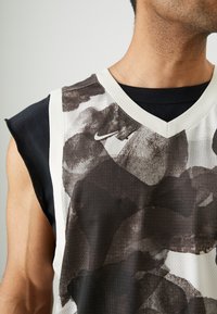 Jersey sin mangas en blanco y negro con un patrón de acuarela abstracto, que presenta un escote en V y una capa interior negra en contraste. Incluye el logo de Nike.