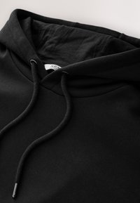 Sudadera negra con capucha que presenta un cuello curvado, cordones ajustables y una textura suave. El interior tiene un tejido liso con una etiqueta visible.