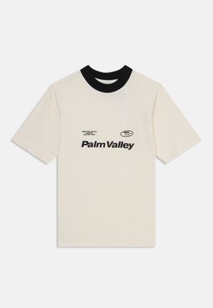 Beżowa bawełniana koszulka z krótkim rękawem z czarnym prążkowanym kołnierzykiem i czarnym nadrukiem "Palm Valley" na przodzie.