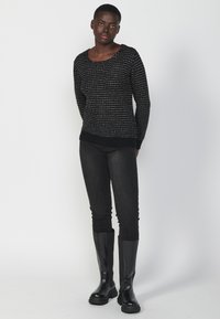 Maglione nero in maglia con texture e scollatura rotonda, abbinato a jeans neri slim e stivali neri fino al ginocchio. Design semplice e moderno.