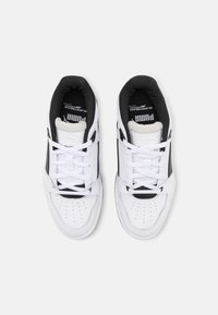 Paire de baskets Puma blanches et noires avec lacets, vue de dessus sur un fond clair uni.