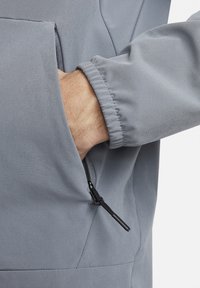 Helehall hall jope, millel on lukuga tasku, elastsed mansetid ja sile, matt kangapind. Disainil on minimaalsed õmblused ja aktsendid.