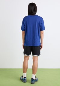 T-shirt en coton bleu à manches courtes et à coupe décontractée, associé à un short en mesh noir avec des accents blancs et des baskets.