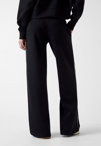 Czarne spodnie dresowe o luźnym kroju, teksturowanej tkaninie, wysokim stanie i bocznych rozcięciach przy nogawce. Minimalistyczny design i jednokolorowy odcień.