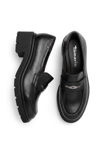 Μαύρα δερμάτινα loafers με χοντρές σόλες, με λουράκι με μεταλλική λεπτομέρεια και το όνομα της μάρκας Tamaris στο εσωτερικό.