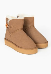 Hnědé semišové kotníkové boty s měkkou ovčí podsadou, plochou světle hnědou podrážkou a ozdobným oranžovým knoflíkem na boku.