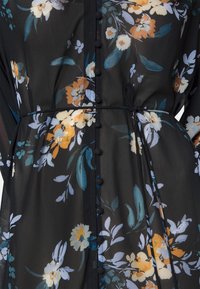 Robe noire transparente avec des motifs floraux bleus, blancs et orange, présentant des boutons recouverts de tissu sur le devant et une fine ceinture à la taille.