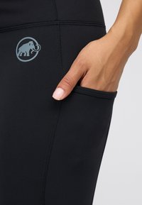 Czarne legginsy wykonane z elastycznego materiału, z boczną kieszenią. Posiadają szare okrągłe logo z wzorem mamuta oraz płaskie szwy.