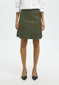 Oliwkowa skórzana mini spódnica z dopasowaną talią, w kształcie litery A, z przeszyciami. Połączona z czarnymi szpilkami z zaostrzonym noskiem.