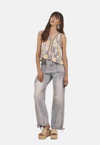 Top sin mangas ajustado y multicolor con diseño estampado; combinado con jeans de pierna ancha de lavado claro, con dobladillo deshilachado y acentos en los laterales.