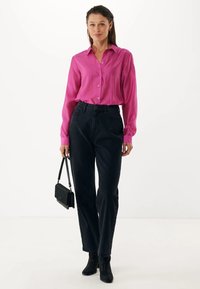 Camisa de botones de manga larga color rosa brillante, combinada con pantalones de mezclilla negra de tiro alto y botas negras hasta el tobillo. Se incluye un pequeño bolso negro.
