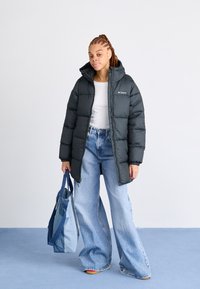 Svart boblejakke med hette, quiltet design og glidelås foran; kombinert med lyseblå vide jeans og en to-farget tote bag.