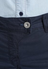 Närbild av mörkblå byxor med knappen fastknuten över en ljusblå skjorta med en mörkblå knapp.