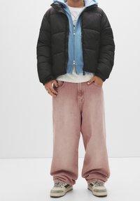 Sort polstret jakke, lyseblå hættetrøje, hvid t-shirt og lyserøde viddebukser. Beige sneakers med mørke detaljer. Minimalistisk baggrund.