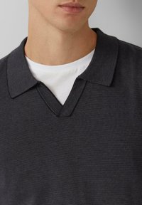 Donkergrijze poloshirt met een gestructureerd patroon, voorzien van een V-halskraag en een gelaagd wit T-shirt met ronde hals eronder.