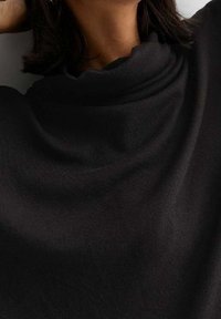 Black top made of soft fabric with a draped neckline, featuring smooth texture and minimal detailing. The design is simple and elegant.