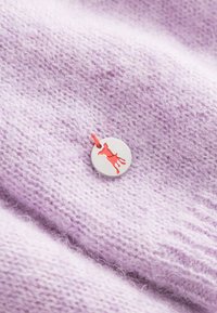 Lila gebreide stof met een fijne, zachte textuur heeft een ronde label. Het label is zilver met een kleine rode hondensilhouet en een oranje touw.