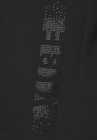 Black fabric top featuring a design of varying sizes of black and silver rhinestones arranged vertically, creating a textured pattern.