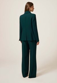 Saco oscuro verde con un blazer estructurado y pantalones de pierna ancha, hecho de una tela suave con un diseño limpio y minimalista.