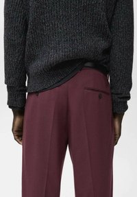 Jersey de punto gris oscuro con bajo redondeado, combinado con pantalones de pinzas granates con bolsillos laterales y un sutil detalle de botón.