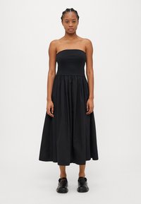 Svart off-shoulder kjole med tettsittende liv og voluminøs, rynket skjørt. Glatt, lett stoff med matt overflate.